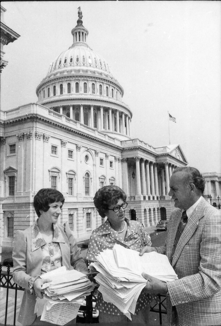Black and white image of three people holding stacks of papers
