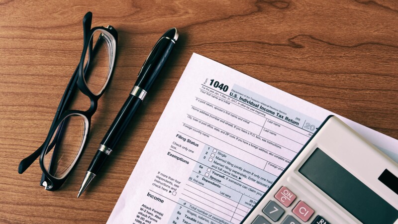 1040 tax document with a calculator on top and glasses and a pen on a table