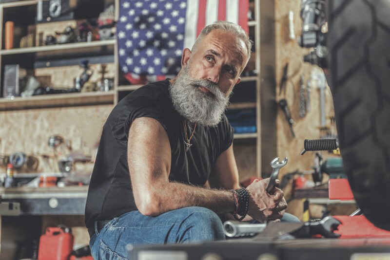 thoughtful mature man holding tool in repair shop