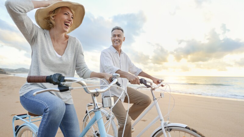 Mature couple cycling on the beach at sunset or sunrise.