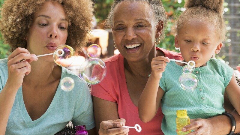 Black multi-generation family blowing bubbles outdoors