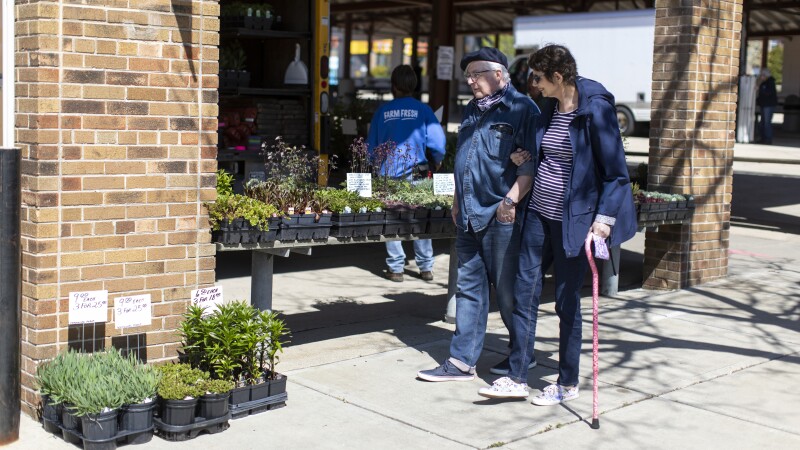 A older man and woman walk past a shop with plants for sale