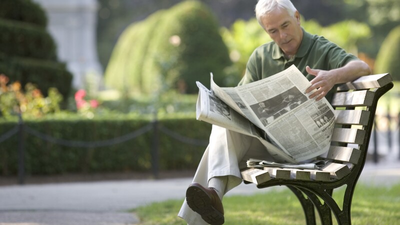 Senior man reading newspaper on park bench, Boston, Massachusetts