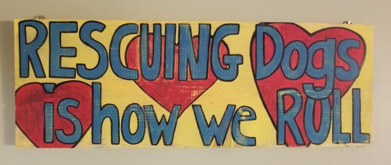 Yellow sign with red hearts and text "rescuing dogs is how we roll"