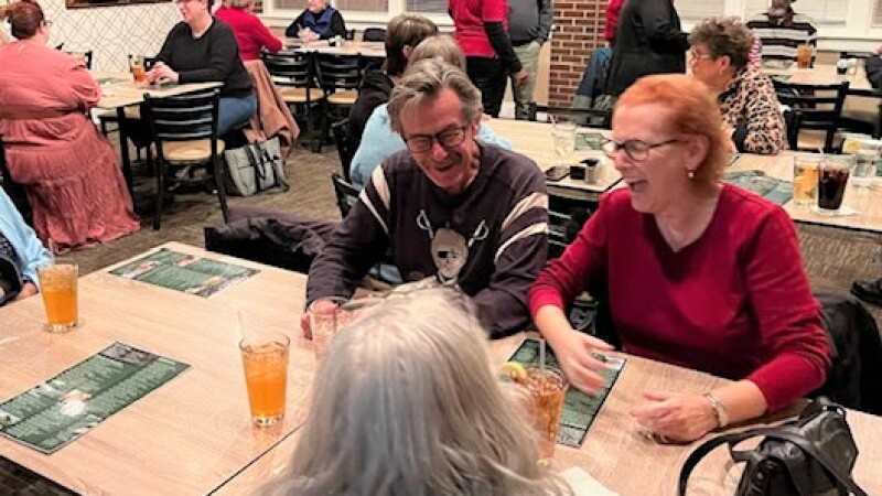 Multiple people sitting at a dinner table socializing and laughing over sweet tea.