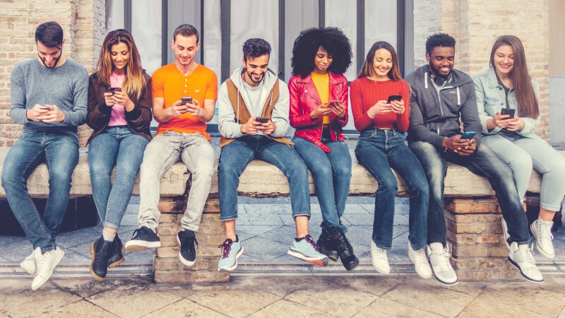 Group of multiracial young people sitting outdoors and watching down to his smartphones