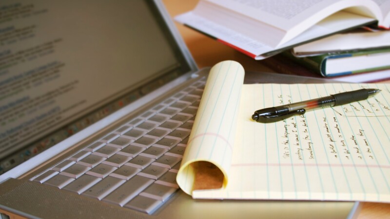 Laptop computer with books, pen and yellow legal pad