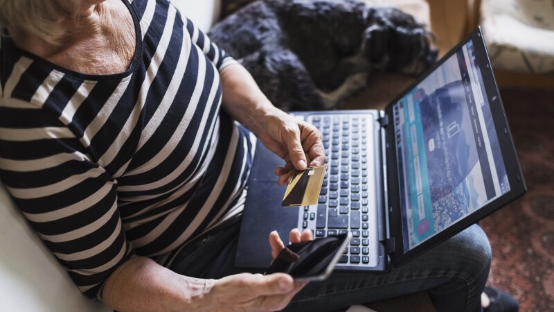 High angle view of senior woman with technologies and credit card sitting by dog on sofa