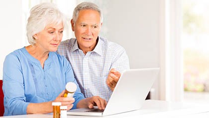 Senior Couple With Pill Bottles Browsing Internet On Laptop.
