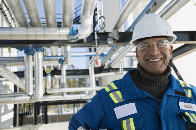 Portrait smiling male worker below gas plant pipeline