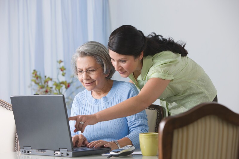 Hispanic woman showing senior mother how to use laptop