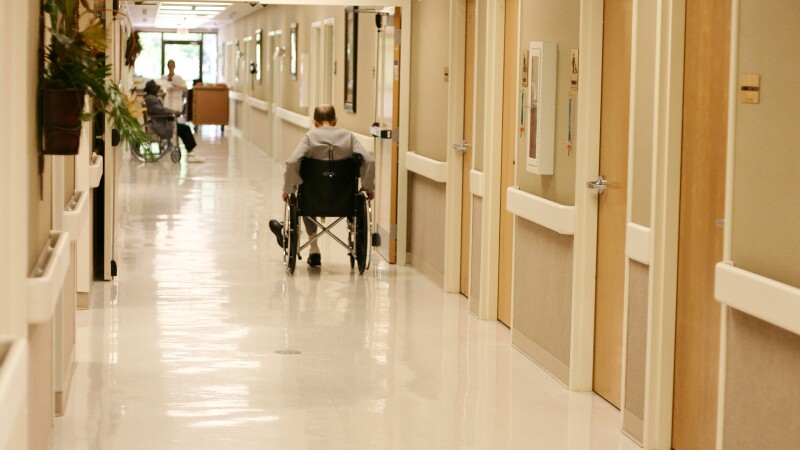 A man in a wheelchair in a nursing home hallway