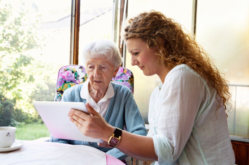 caregiver helps senior woman use digital tablet