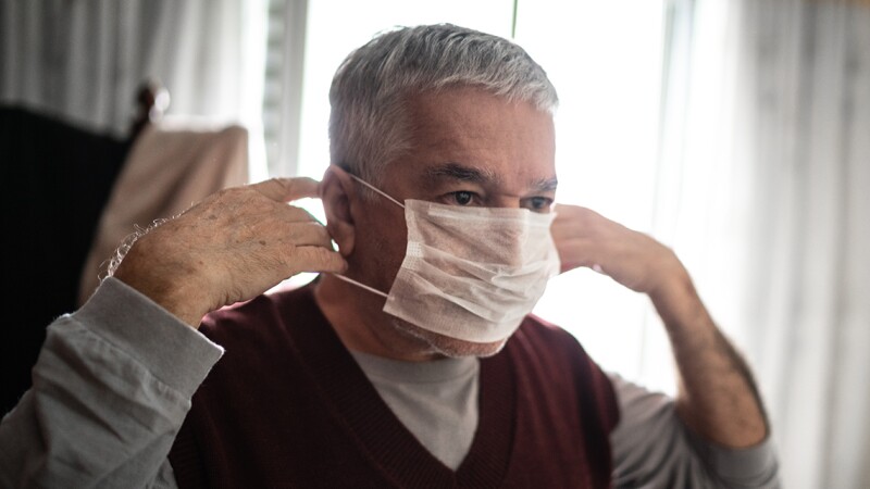 Senior man putting on a protective mask for coronavirus at home