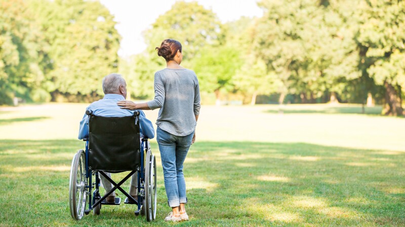 Senior man sitting on a wheelchair with caregiver