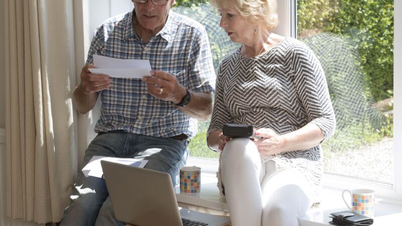 Moving house. Couple sitting on a window seat opening an account to be settled before completion of the sale.