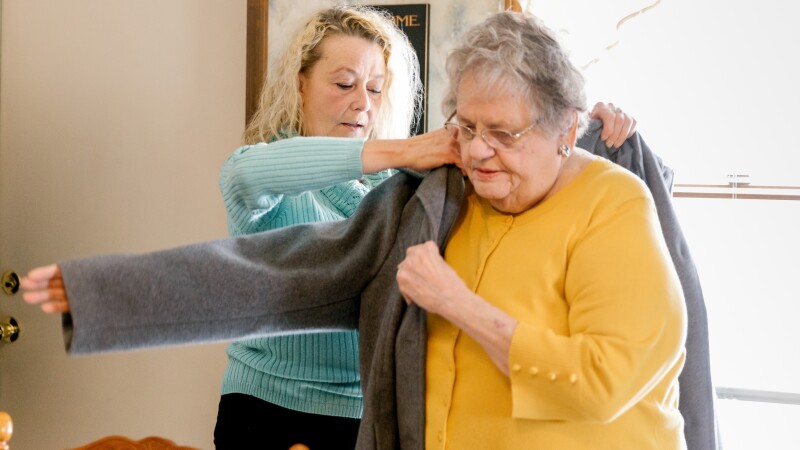 A woman helps her elderly mother put on a coat