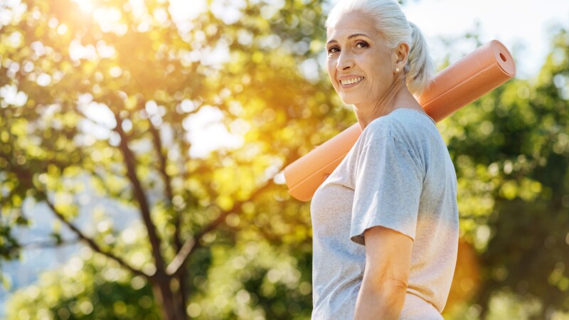 Cheerful senior woman going to enjoy yoga in the park