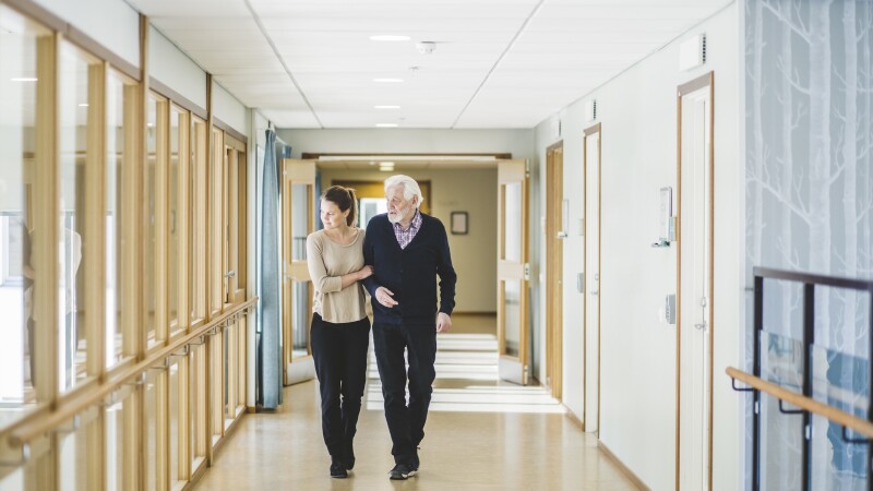Young woman looking away while walking with grandfather in corridor at nursing home