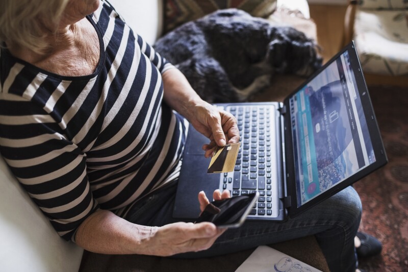 High angle view of senior woman with technologies and credit card sitting by dog on sofa
