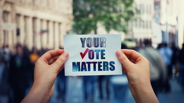 Hands hold a paper sheet with the message your vote matters over a crowded street background. People legal and democratic rights, every voice counts. Election campaign and electoral agitation concept