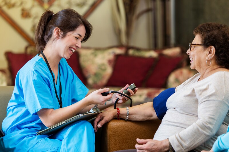 Smiling nurse checks senior Hispanic woman's blood pressure