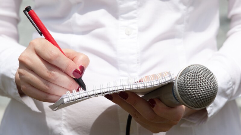 Female journalist at news conference, writing notes, holding microphone