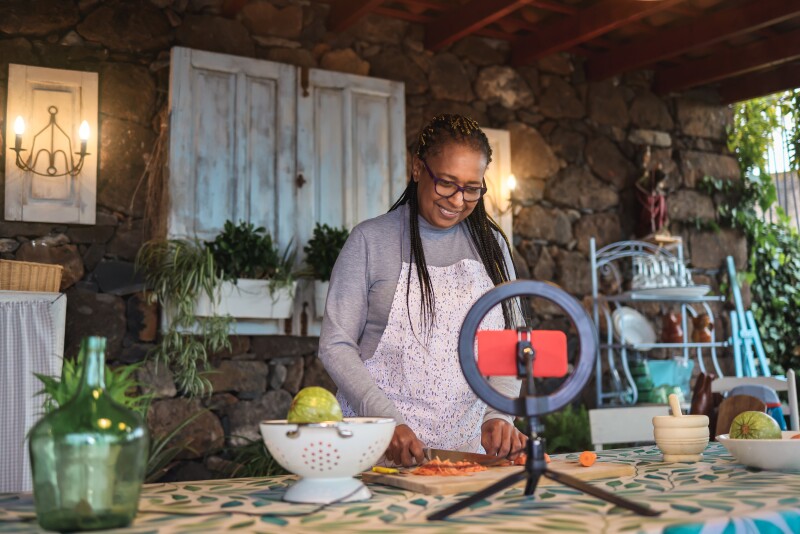 African senior woman streaming online virtual masterclass cooking lesson outdoors at home - Focus on face