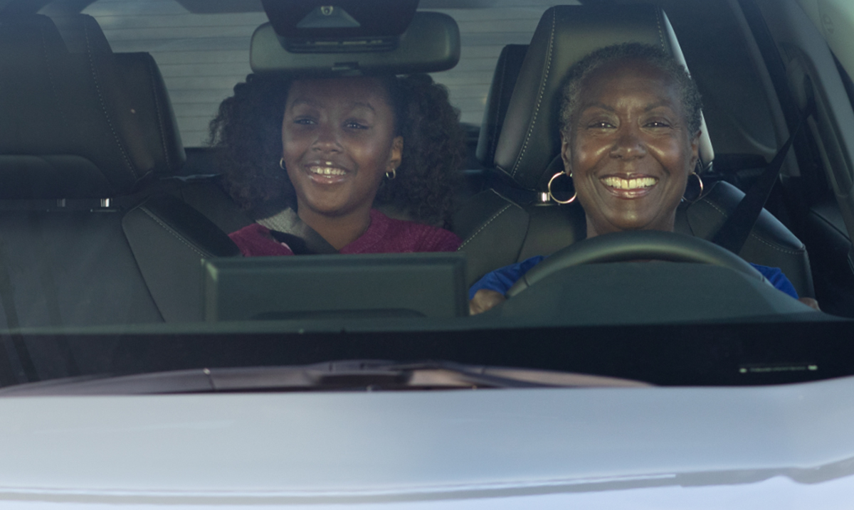 Older woman driving car with girl in back seat.