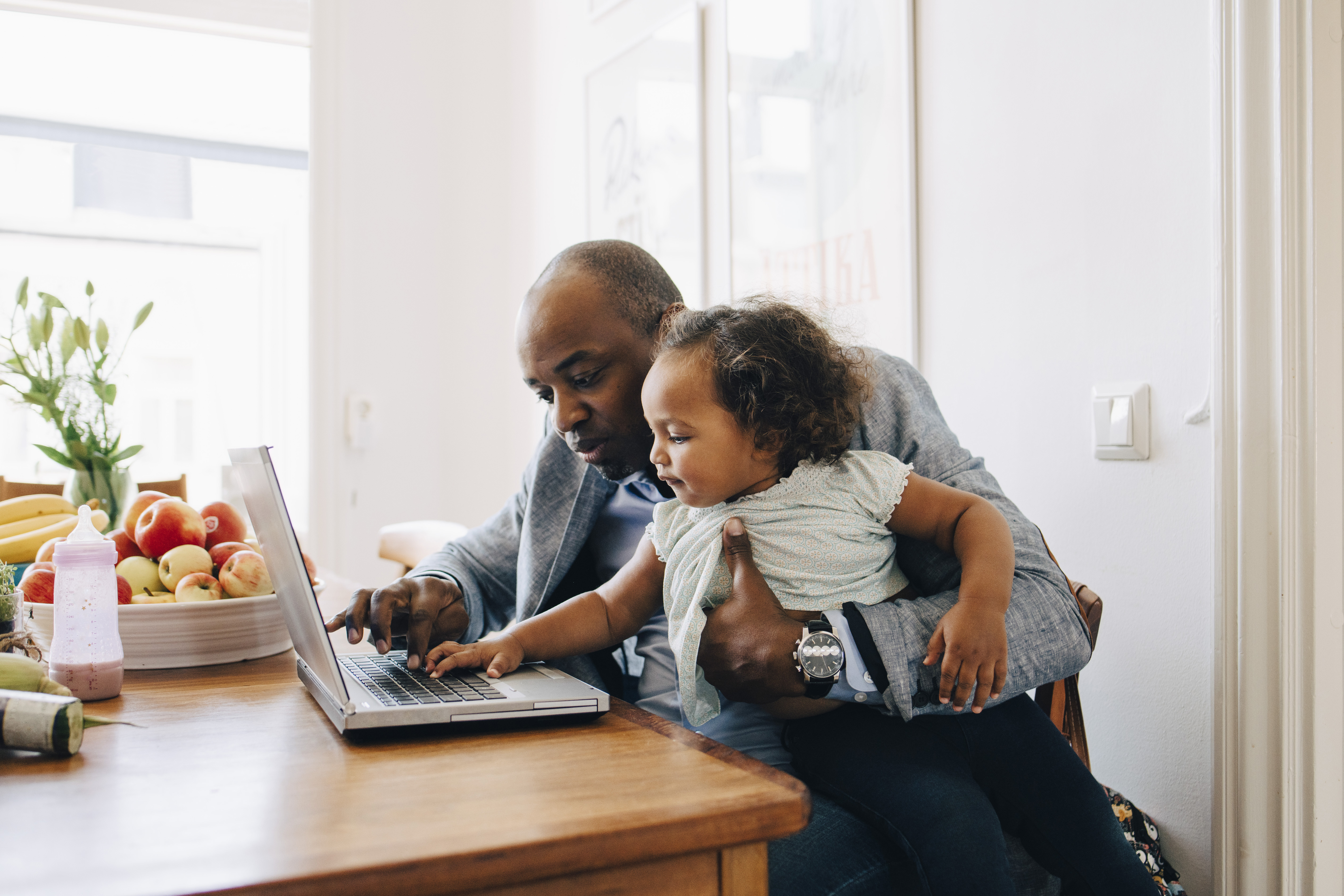 Father showing laptop to daughter while sitting at table in dining room