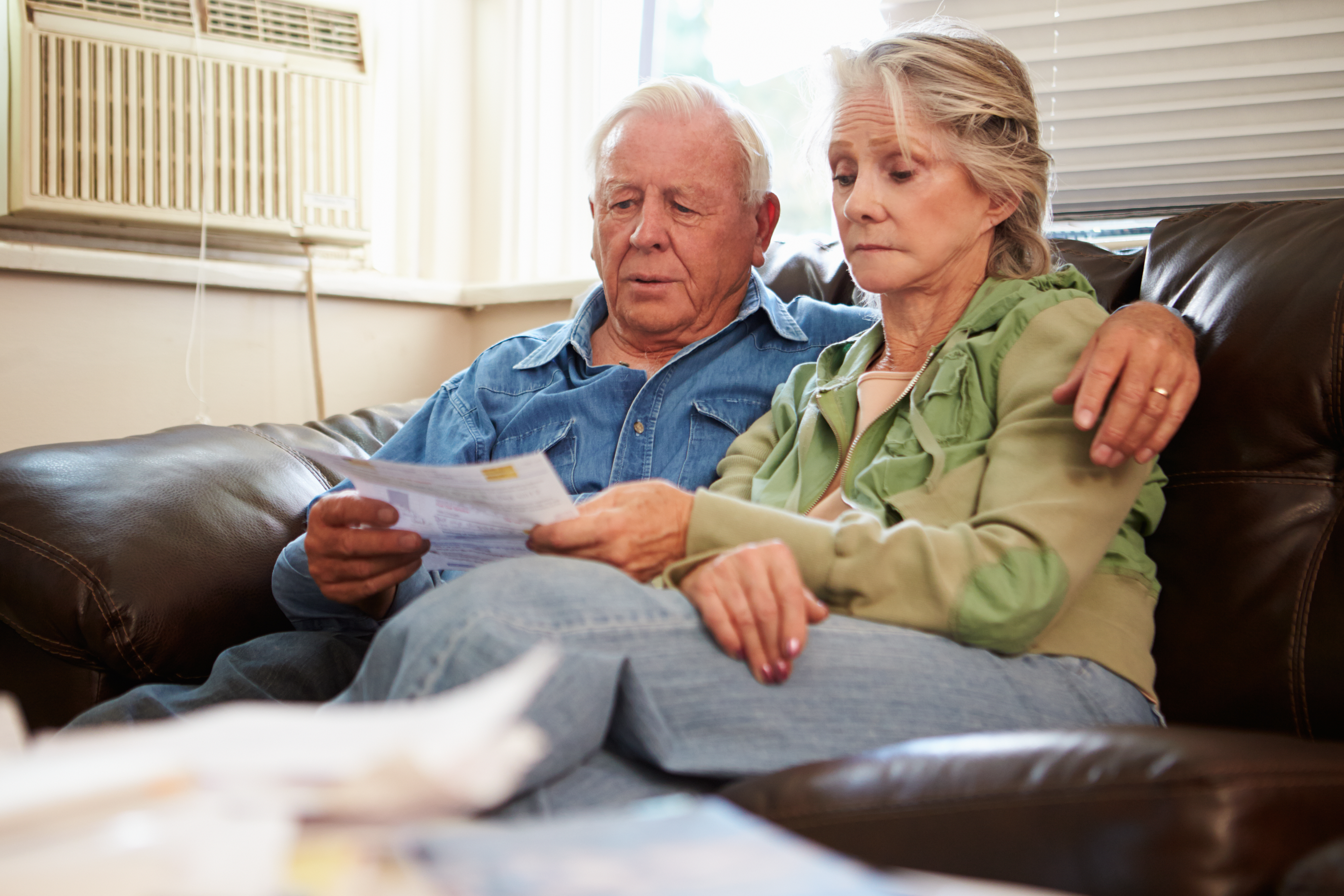 Worried Senior Couple Sitting On Sofa Looking At Bills