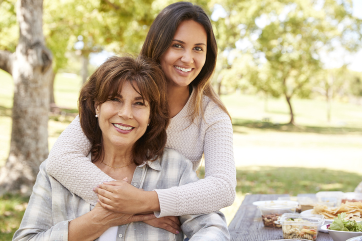 Senior mother and adult daughter embracing in park, close up