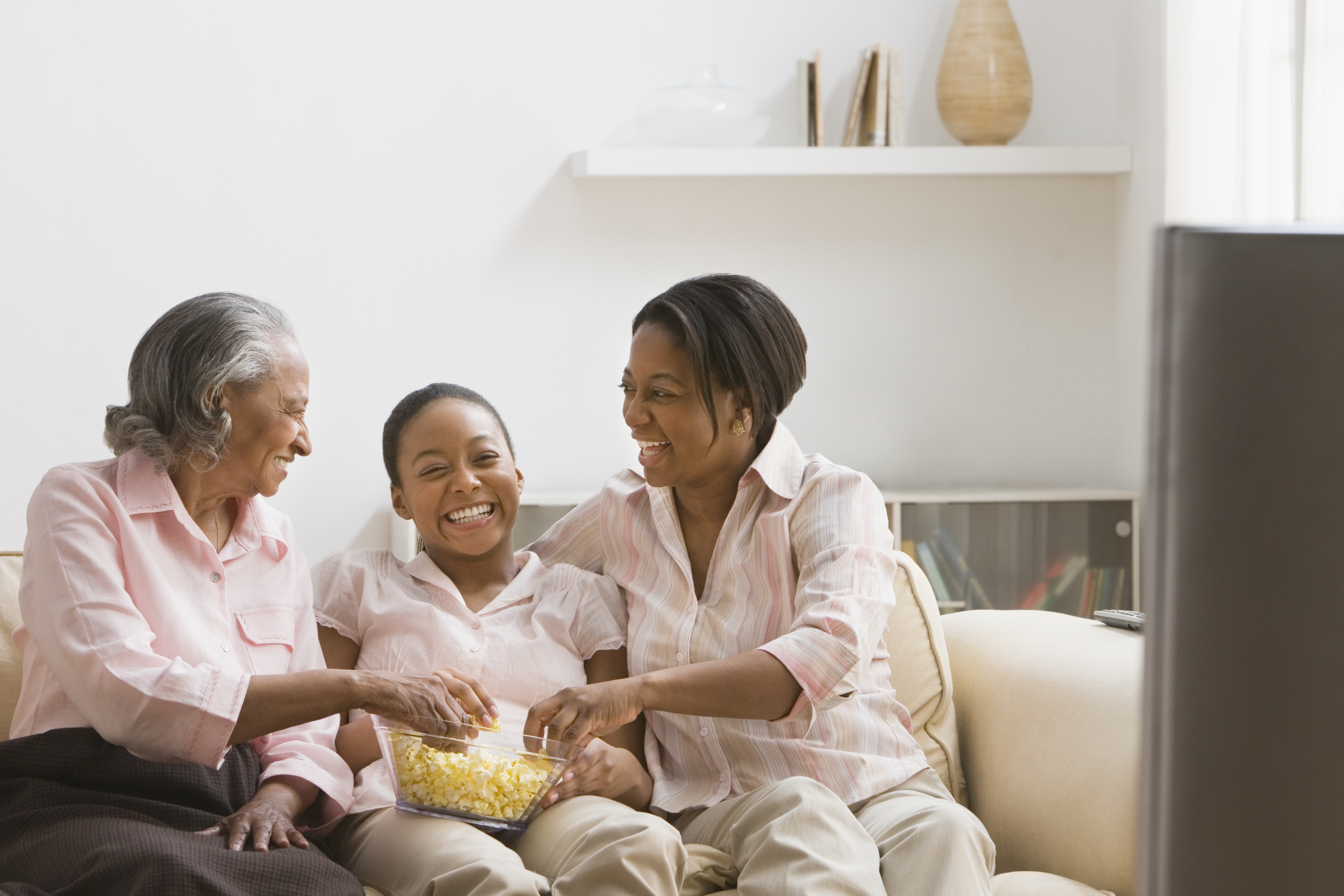 Three generations of African women eating popcorn on sofa