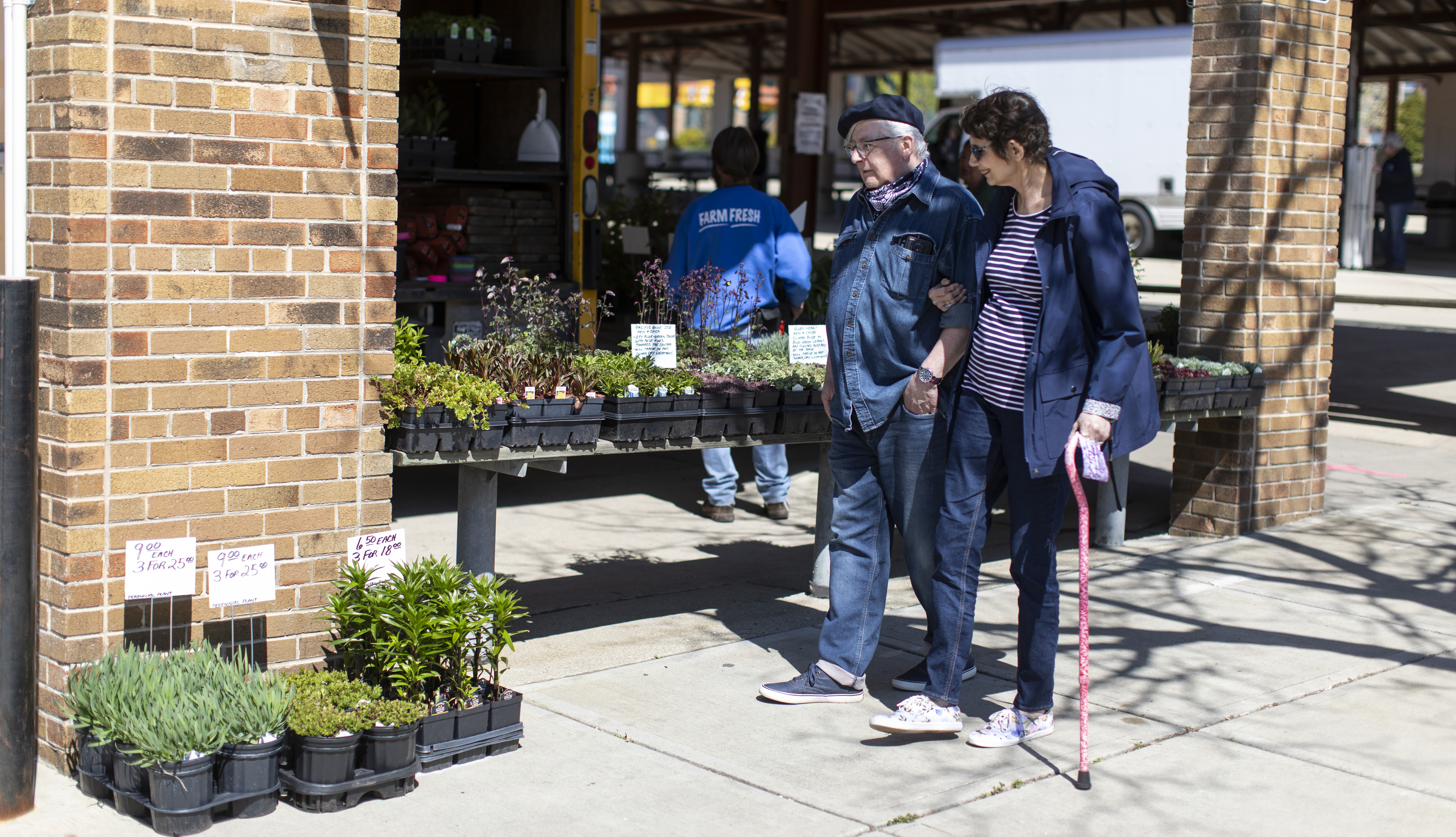 A older man and woman walk past a shop with plants for sale