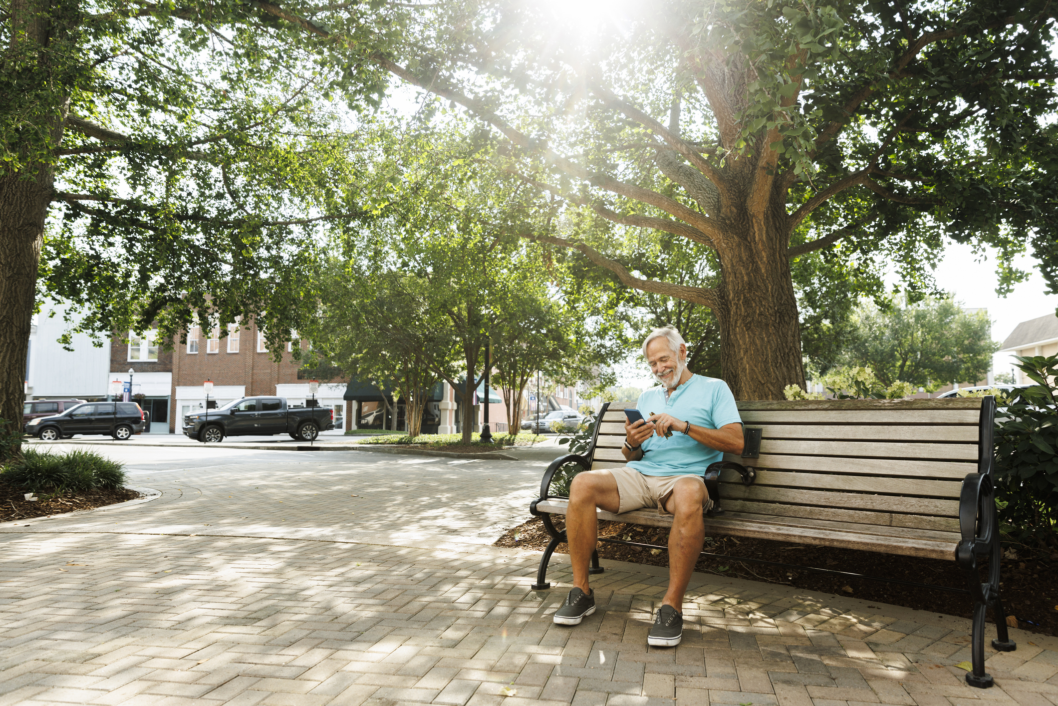 Cheerful senior man using smart phone while sitting on park bench