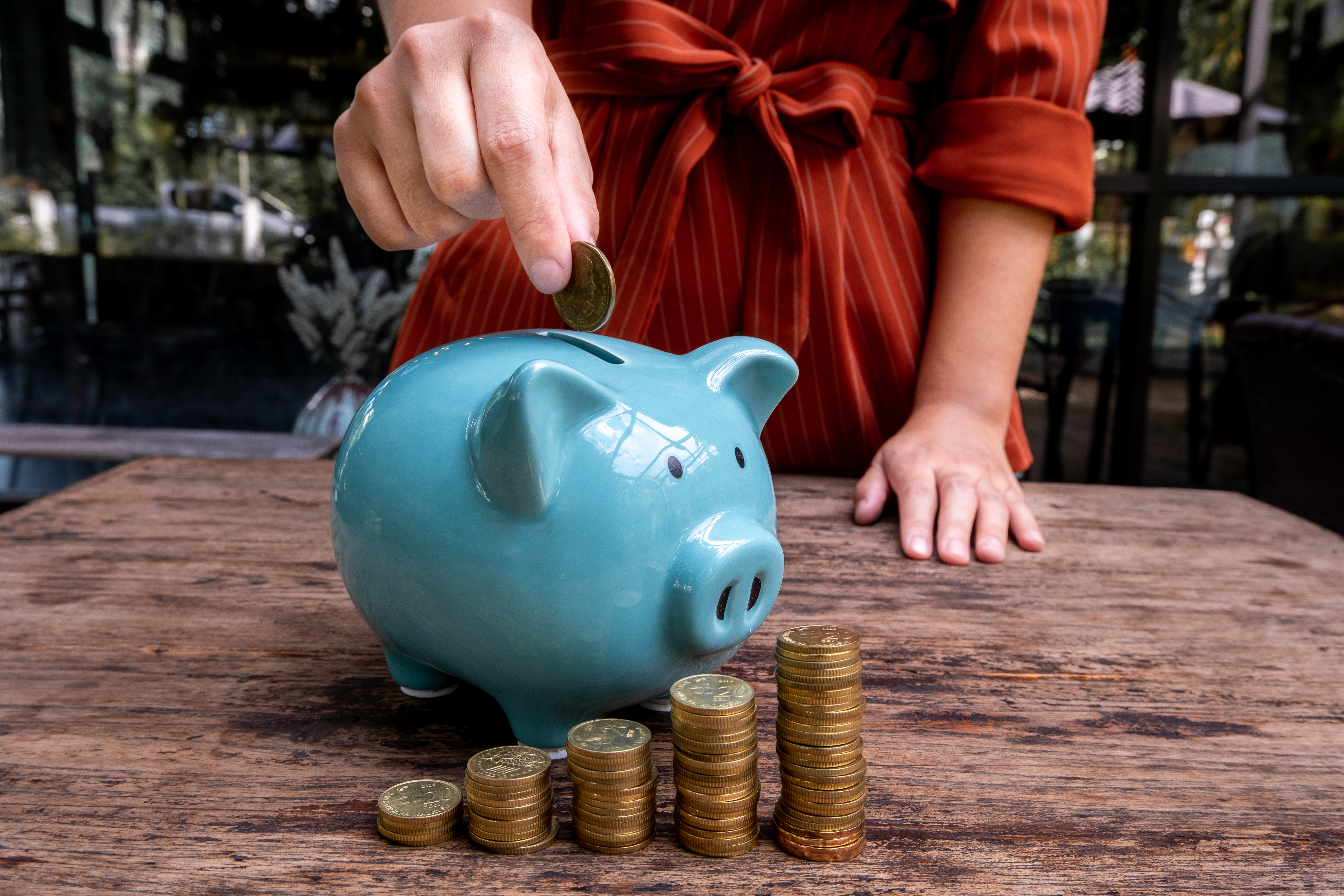 Midsection Of Woman Putting Coin In Piggy Bank On Table