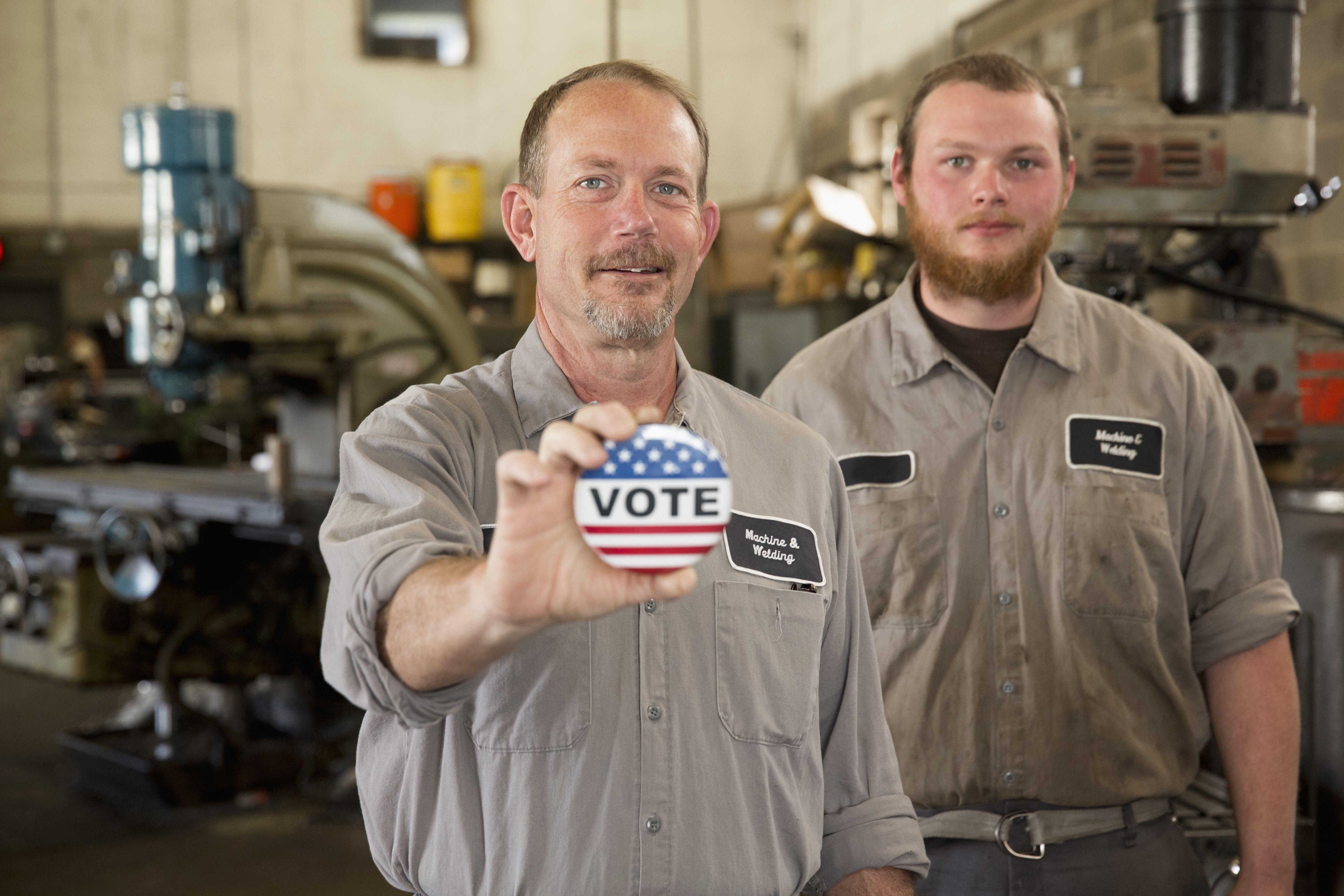 Caucasian machinists holding Vote' button in garage
