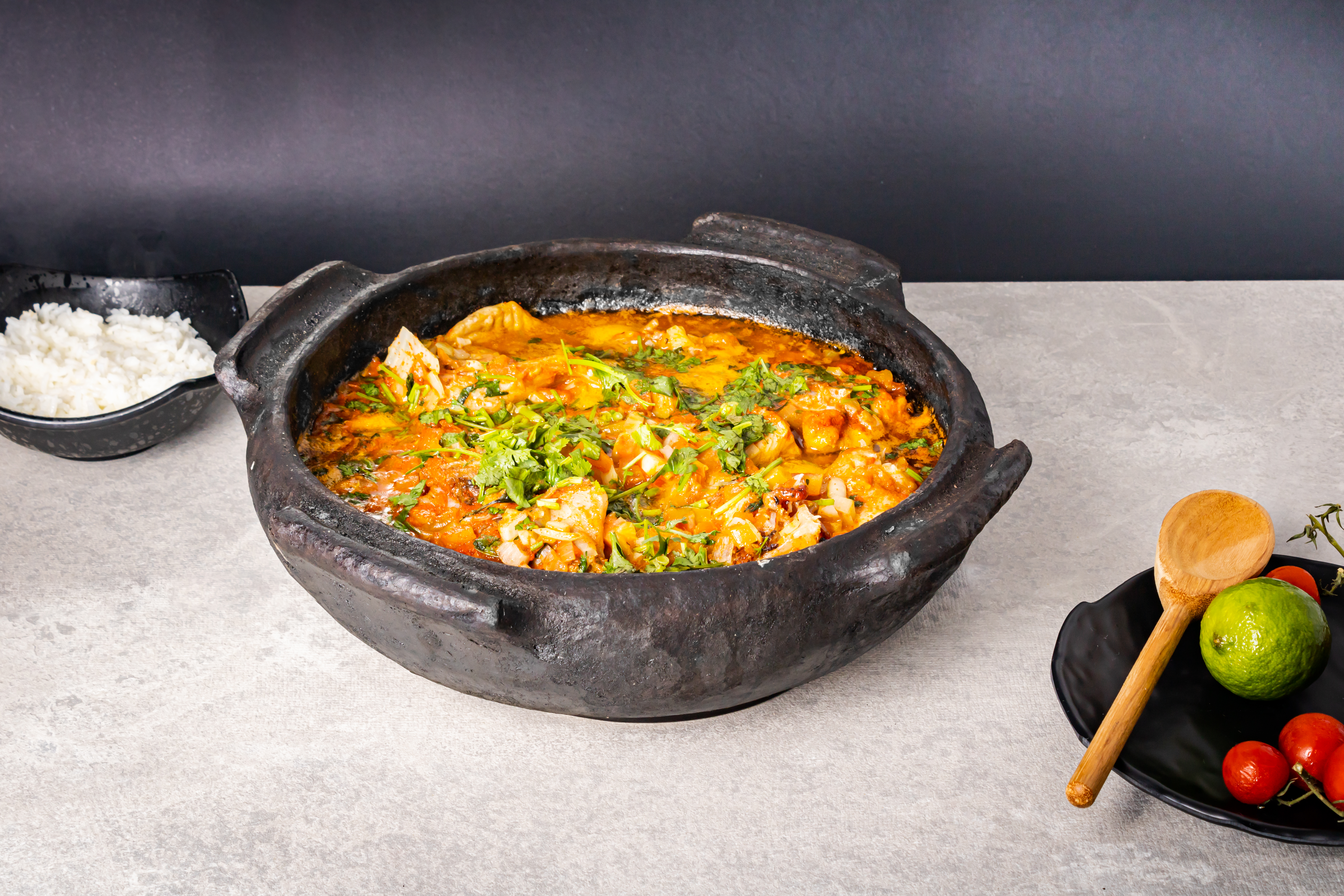Delicious Brazilian fish moqueca with tomato, onion, olive oil, coriander and orocum seed. Made in clay pot on white table and black background.