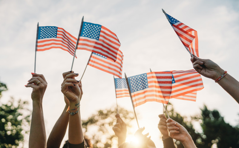 A group of people is waving small American flags at sunset