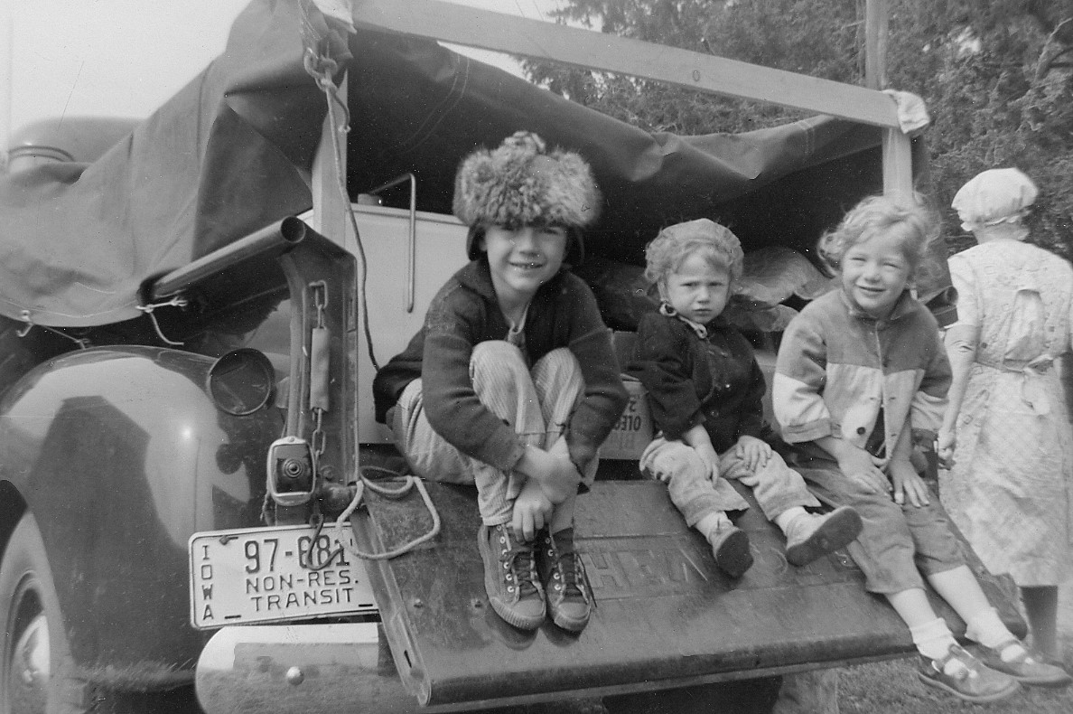Black and white image of three children sitting in the back of a truck