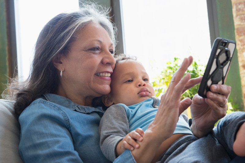 Hispanic grandmother holding grandson and texting on cell phone